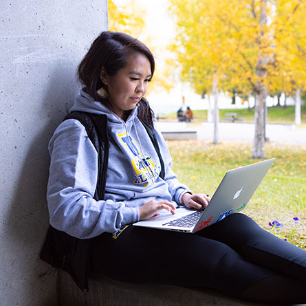 A student with a laptop studies outside the Gruening Building on the UAF campus